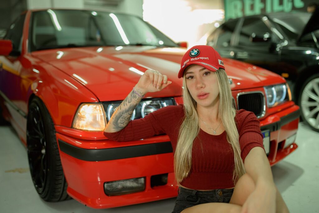 Woman posing casually with a red sports car in a garage setting.