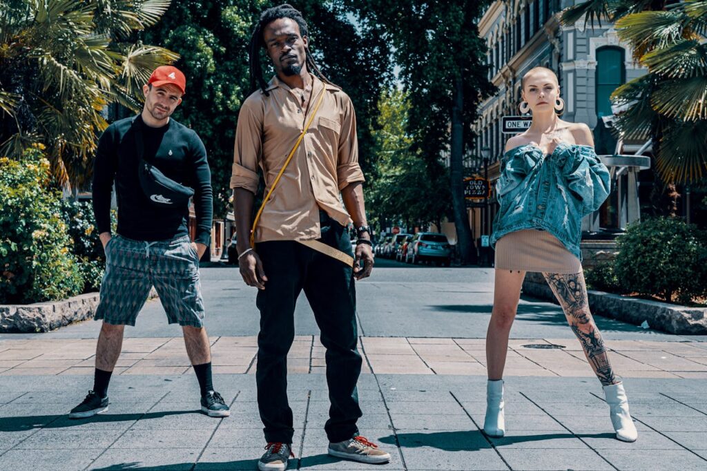 Three stylish individuals posing confidently on a sunny urban street, showcasing modern fashion trends.