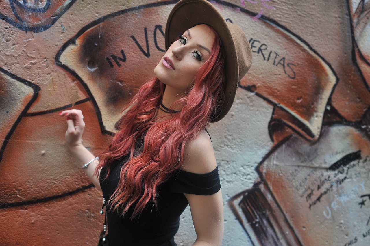 Stylish woman poses against a vibrant graffiti wall, wearing a fedora and chic outfit.